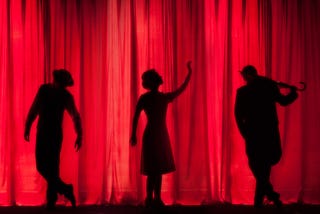 three black silhouettes against a red drapery background