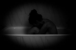 Woman hunches over in a bath tub.