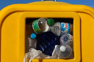 A bright yellow trash can filled with empty plastic bottles and plastic waste.