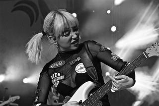 Blonde haired girl in black top playing a Fender Stratocaster electric guitar on stage