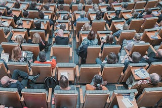 An overhead wide shot of a crowded lecture hall from the back of the room.