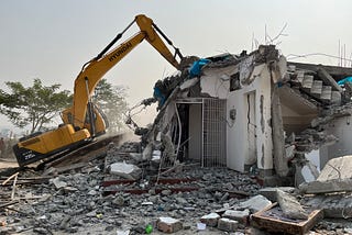 A yellow backhoe pulling down the remains of a building.