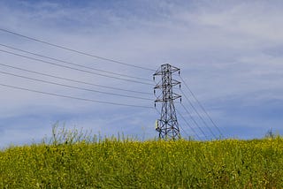 Photo electricty pylon in a green field below a blue sky.