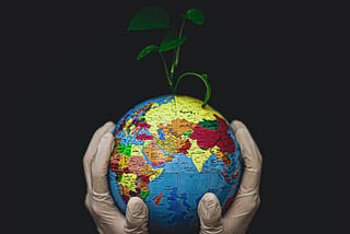 Gloved hands tenderly holding a globe of the Earth with a seedling shooting out of the top of it.