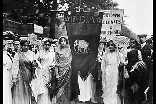 Image description: A black and white photo of Indian suffragettes at the 1911 Coronation Procession holding a triangular flag with the word India and an elephant beneath.