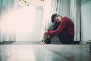 A young person sits alone in the corner of a room