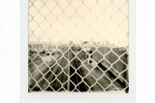 sepia toned polaroid picture of train tracks through fence