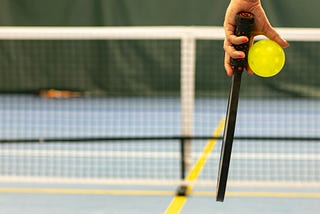 Person holding pickleball paddle and ball in front of net