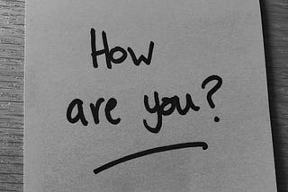 Black and white photo of a Post-it note with ‘How are you?’ written in black marker