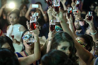 Women raise wine glasses and cheer, some masked.