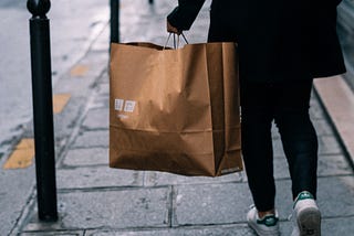A person walking away carrying a large brown paper bag with the Uniqlo logo.