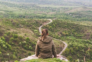 Woman sitting on a hill looking over a long winding road.