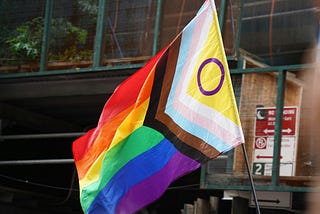 Progress pride flag waving in front of a building with the hoist on the right