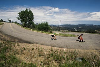 Two skateboarders on a downhill road at a hairpin turn