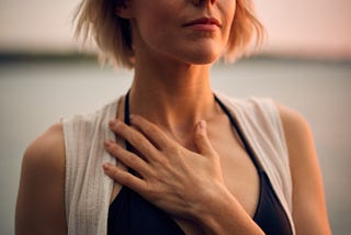 A calm looking person in a meditative state with eyes closed and left hand placed on the chest