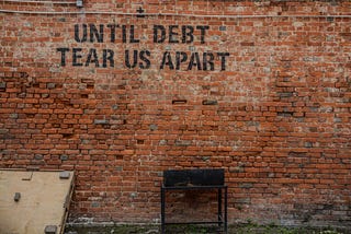 This is a picture of a brick wall with the words, “Until Debt Tear Us Apart” written on it.