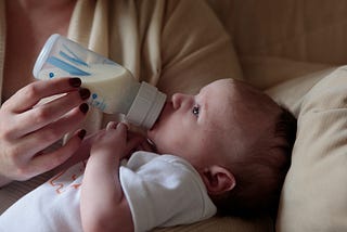 A mother embracing her baby while feeding her a bottle of formula.