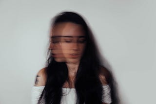 Blurry photo of a woman with black hair and a white shirt looking down and to the side.
