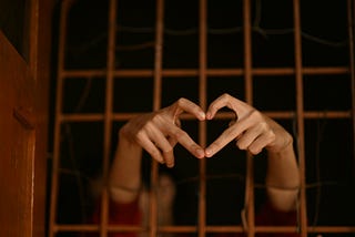 Hands reaching through a prison gate forming a heart