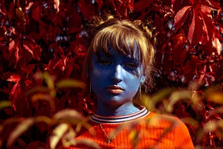 A photo portrait of a woman with blue skin and strawberry orange hair with red leaves surrounding her.