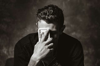 A man covering his face with a wad of cash, looking slightly depressed