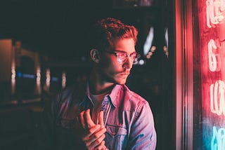 A man in front of some neon lights, holding his own hand.