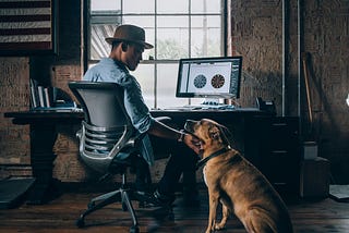 man wearing hat and his dog in front of a computer