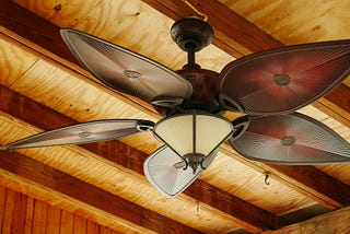 Brown ceiling fan with leaf shaped blades and tan colored light fixture.