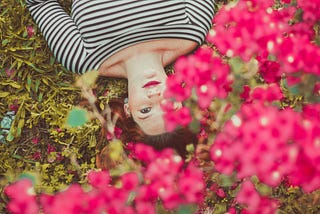 Woman laying down on the grass by some pink flowers