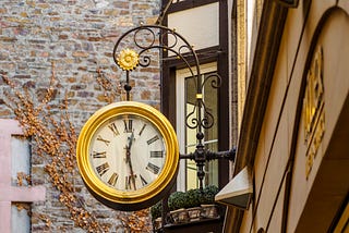 Gold clock hanging outside a brick storefrong