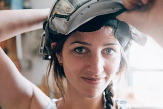 Photo of a woman maker lifting a welding helmet to smile at the camera. Most crafters and makers on handmade marketplaces are women.