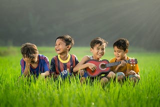 Some young children sitting with a ukulele and looking happy