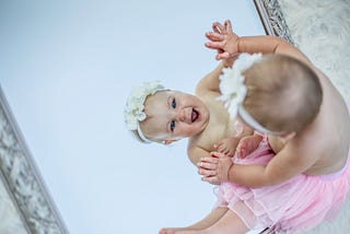 Baby with a flower tiara on looking at herself in the mirror