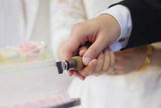 a bride and groom’s hands cutting a wedding cake