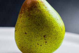 A green pear on a white table.