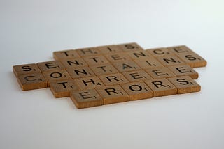 Scrabble game tiles arranged in five rows reading, “This sentence contains three errors.” Alt text to illustrate the importance of alt text.