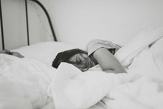 A black and white photograph of a woman asleep in bed, depressed