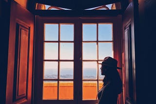 A woman with a hat on looking outside of a window at the sky.