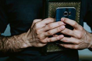 Man wearing dark grey shirt holding journal and phone close to his heart picture