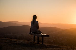 sunrise, someone is sitting on a park bench in the mountains