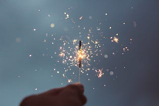 shadow of a hand holding up a sparkler against a dark grey or indigo sky