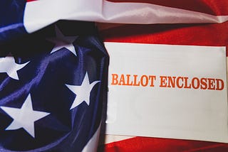 An envelope that says “BALLOT ENCLOSED” in red interlaced with the American flag