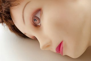 Image of robotic looking head of woman laying down with her eyes wide open but staring unexpressively into the space in front of her.