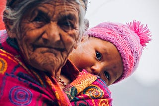 An old wizened woman with a baby peering over her shoulder