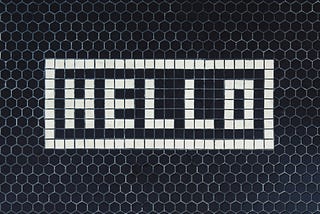 Blue-gray mosaic tile with white tile that spells Hello.