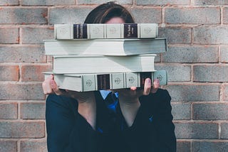 A photo of an individual holding a stack of books in front of their face