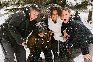 Family of four smiles and laughs in the snow.