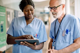 Smiling female nurse showing an electronic health record on a digital tablet to male hospital colleague
