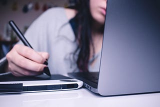 A woman creates digital content with a stylus, drawing pad, and laptop.