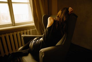 woman curled up on chair by window with her back to us